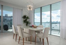 A Dining Room Design In Soft, Neutral Tones Adorned With A Pendant Lighting Fixture, And Featuring A Waterfront View.