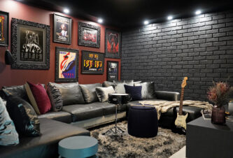 Rock 'n' Roll Inspired Media Room With Curated Art, Deep Maroon Accent Wall, Black Brickwork, And Lounge Sofa, And Musical Instruments.