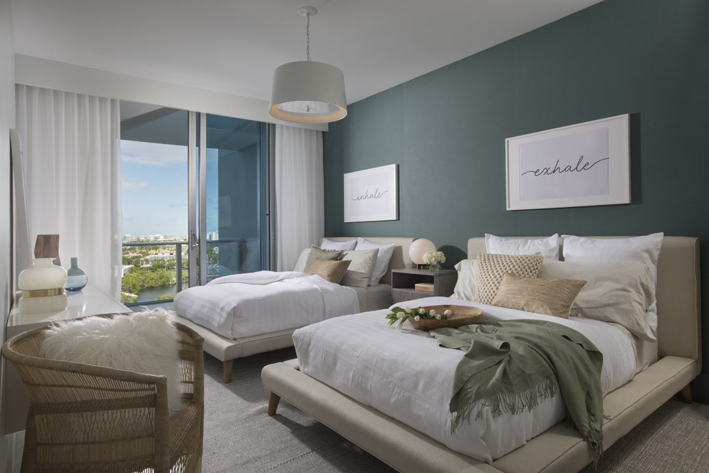 A guest room design with two queen beds, woven side chair, and wall art. 