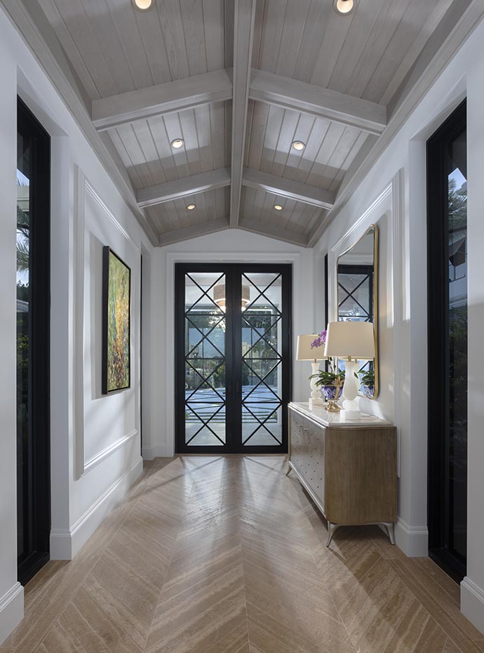 A transitional home entry foyer, adorned with a framed glass door, vaulted ceiling, entryway table, painting, and mirror, showcasing a remarkable before and after.