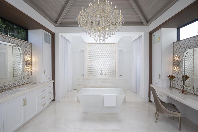 A transitional master bathroom in a home, showcasing vaulted ceilings, a vanity, a walk-in shower, and a  bathtub adorned with an elegant crystal chandelier.